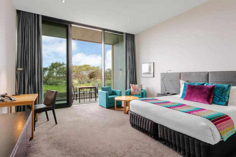 Guest room with a sitting area, a bed, and desk, and balcony at RACV Torquay Resort. 