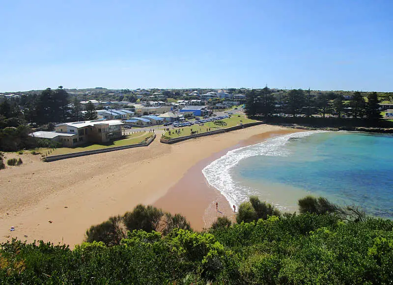 View of Port Campbell Beach and the Surf Lifesaving Club with blue skies and green shrubs in the foreground.