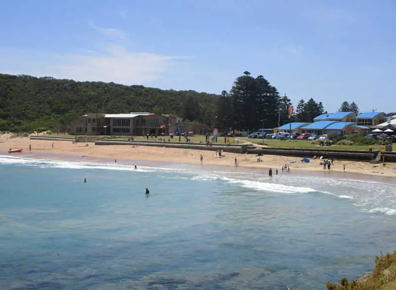 People swimming at Port Campbell beach with a view of the foreshore and Surf Lifesaving Club..