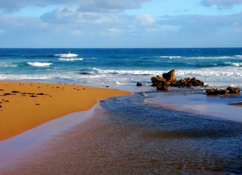 Image of a beach in Warrnambool Australia with rocks, sand, ocean, and blue sky with clouds.