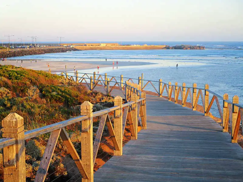 Image of the boardwalk along the Warrnambool foreshore promeande with the ocean, beach, and grey skies.