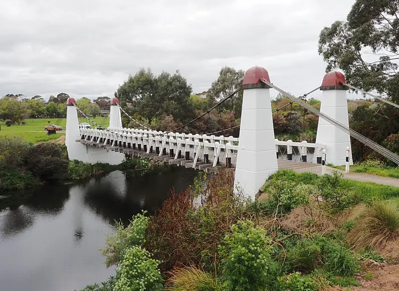 View of the Wollaston Bridge over the Merri River in Warrnambool with white and red pillars and surrounding greenery. One of the free Warrnambool attractions.