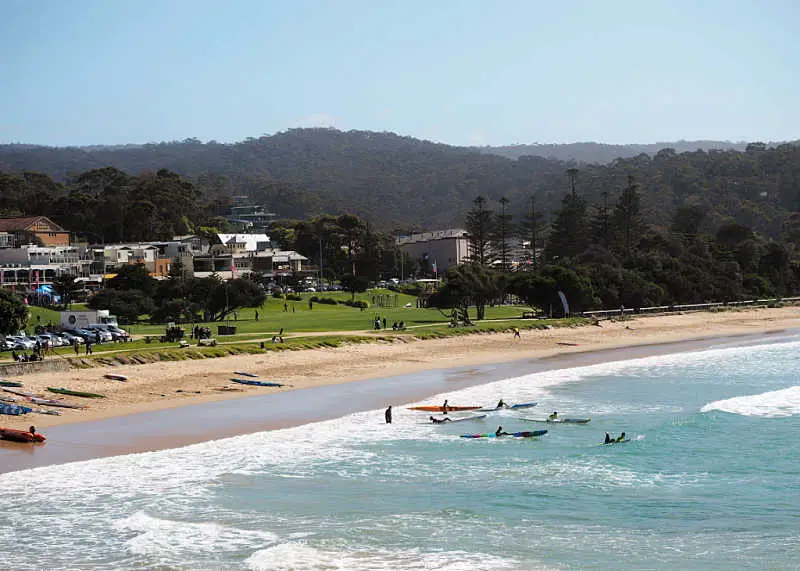 View of kayaks in the water, Lorne beach with the town of Lorne on the Great Ocean Road in the background. 