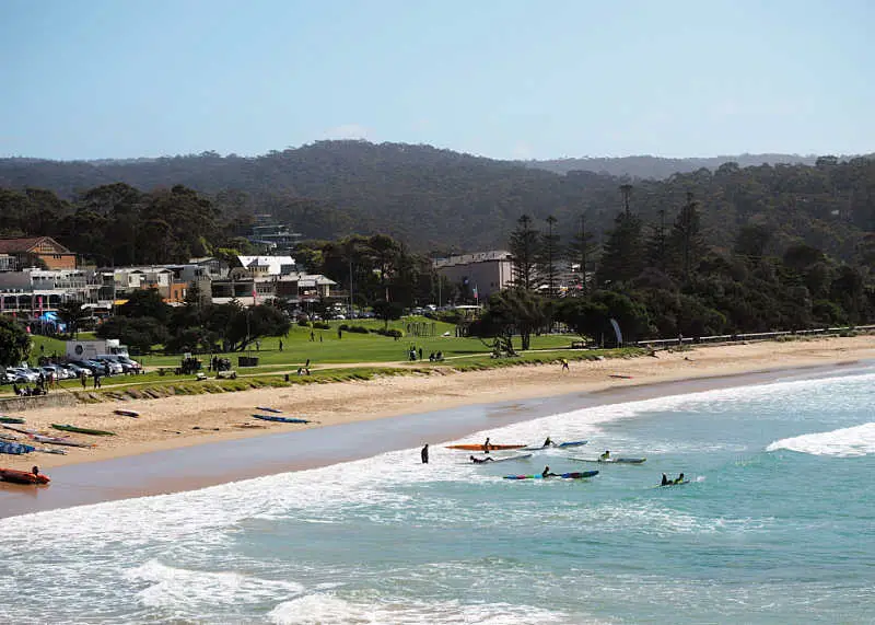 View of kayaks in the water, Lorne beach with the town of Lorne on the Great Ocean Road in the background.