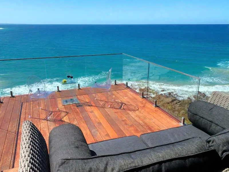 Sunken deck with glass balustrade with a couch and table and chairs overlooking the stunning ocean.