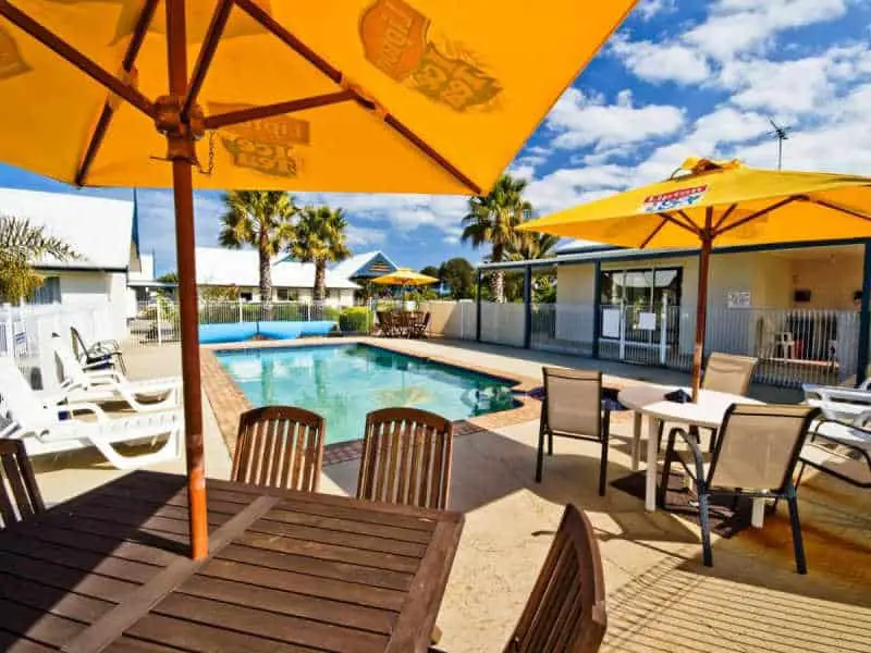 Pool area with tables and bright yellow umbrellas at Tropicana Motel in Torquay Victoria.