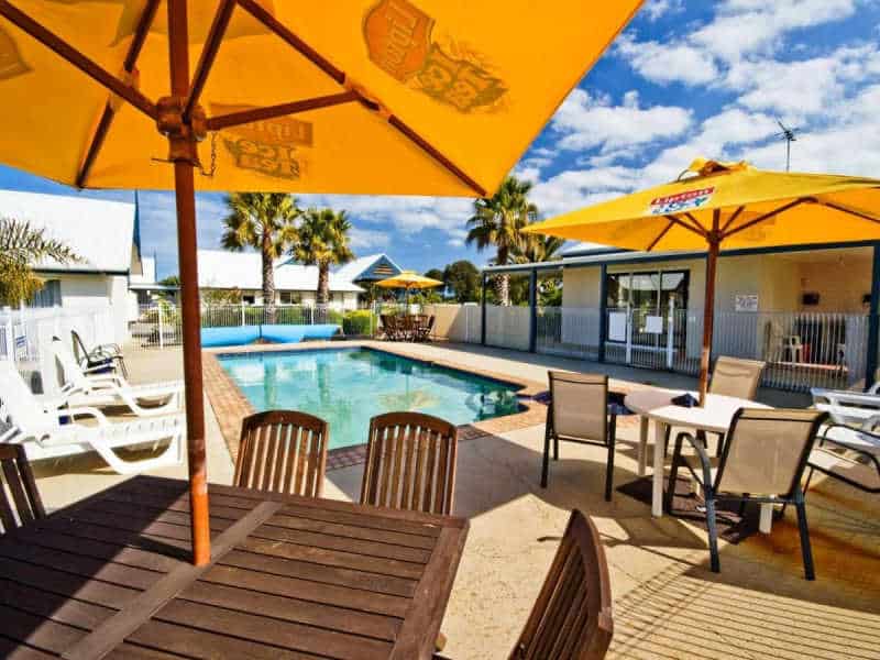 Pool area with tables and bright yellow umbrellas at Tropicana Motel in Torquay Victoria.