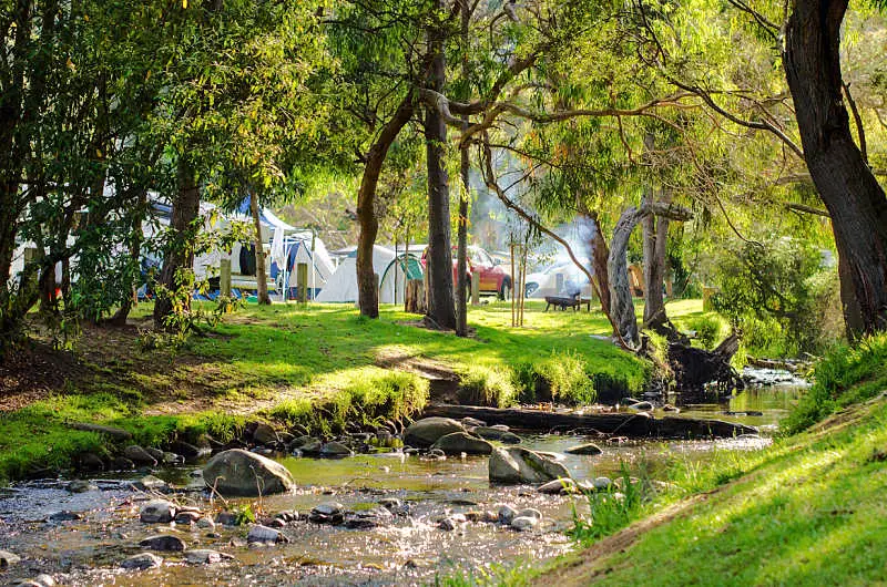 The beautiful riverbank of a small flowing river with some camping tents and fire pits in the background at Wye River, on the Great Ocean Road VIC Australia