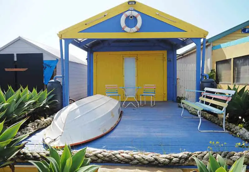 Brightly painted boat shed with verandah, row boat, and seats at Campbell Cove Beach.