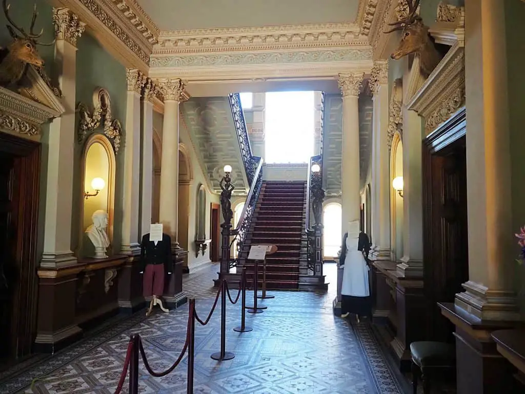 Entrance hall featuring a staircase, pillars, and mannequins wearing traditional clothes.