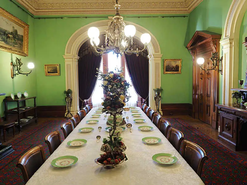 Formal dining room at Werribee Mansion painted green and gold with a set table and chandelier.