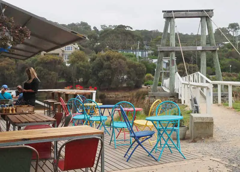 The Lorne Swing Bridge Cafe with colourful tables and chairs sitting beside the Swing Bridge.