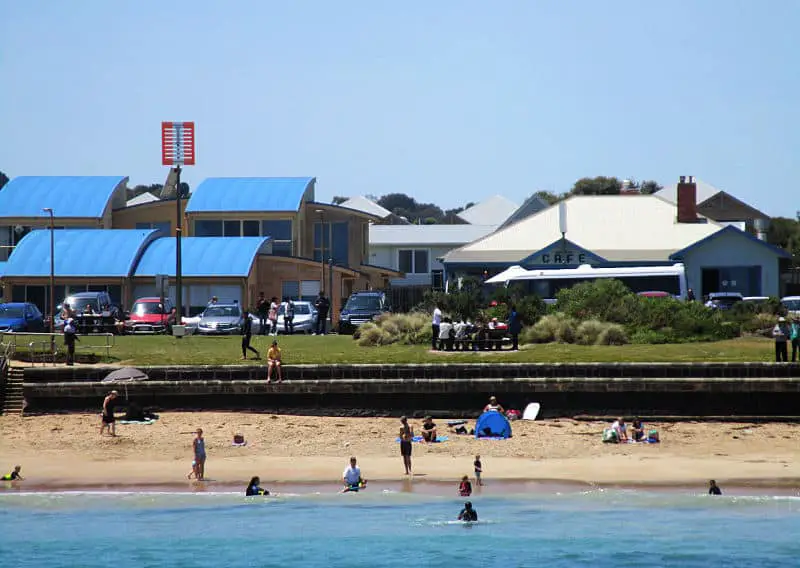 People swimming and enjoying the beach at Port Campbell with the Surf Lifesaving Club and a cafe in the background.