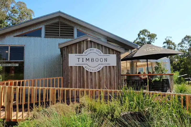 Front entrance to Timboon Distillery with umbrellas, Timboon sign, and greenery.