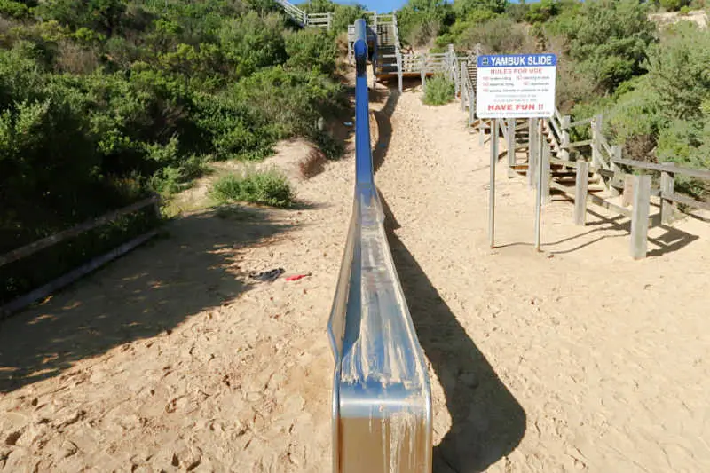 Giant Yambuk Slide surrounded by sand and greenery. With a sign diplaying the rules. One of the fun things to do near Port Fairy Victoria