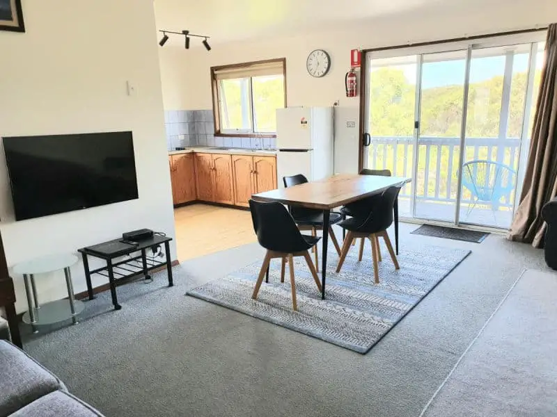Port Campbell Motor Inn living area with a television, table and chairs and a kitchen.