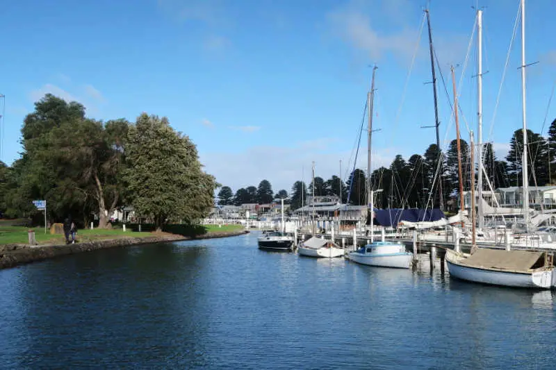 Sail boats moored at Port Fairy Harbour with grass on trees on the banks of the river.