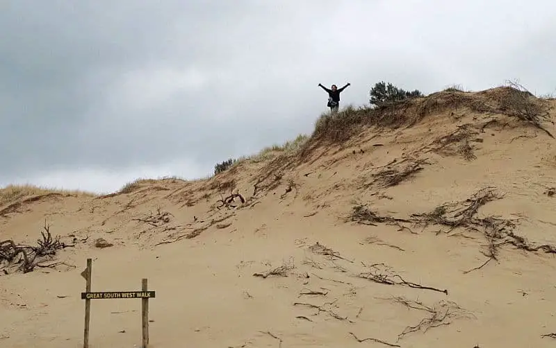 Person standing on top of a sand dune behind a Great South West Walk sign.