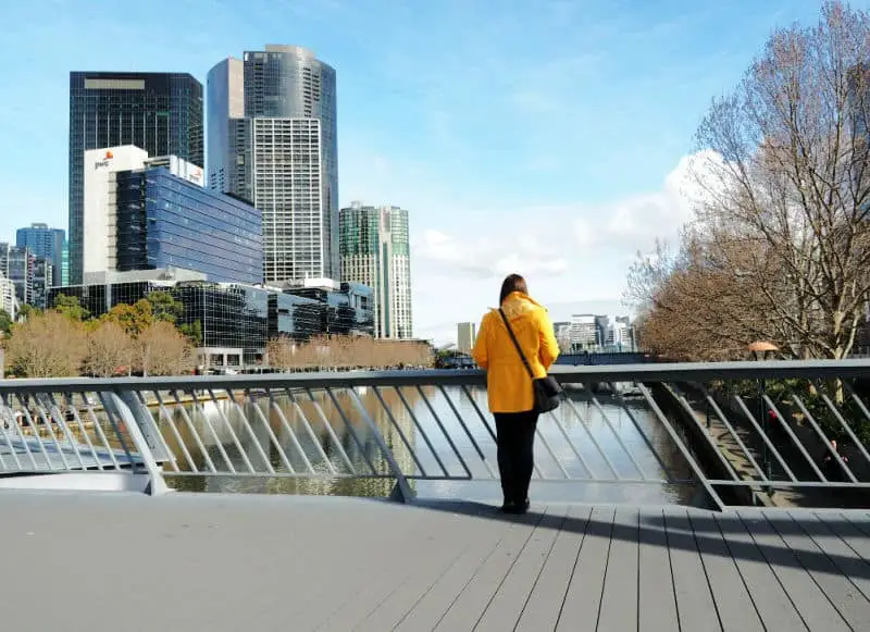 Woman in yellow looking over the Yarra River and Southbank in Melbourne from a bridge.