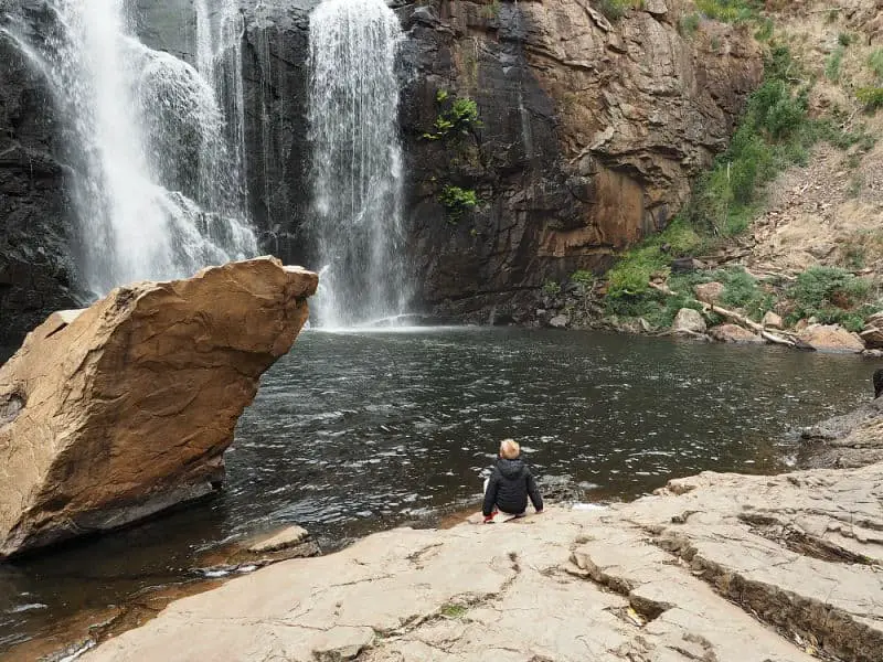 Young boy sitting at the base of MacKenzie Falls in Halls Gap Grampians Victoria.