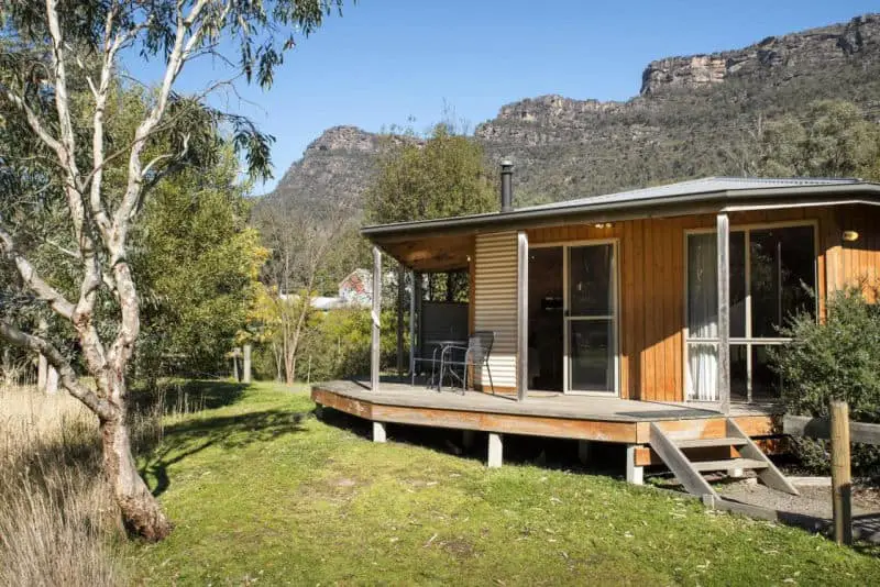 View of a cabin at Halls Gap Chalets with trees and mountains in the background.