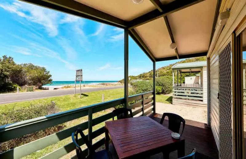 Deck with table and chairs, blue sky, and ocean views at Kennett River Caravan Park on the Great Ocean Road.
