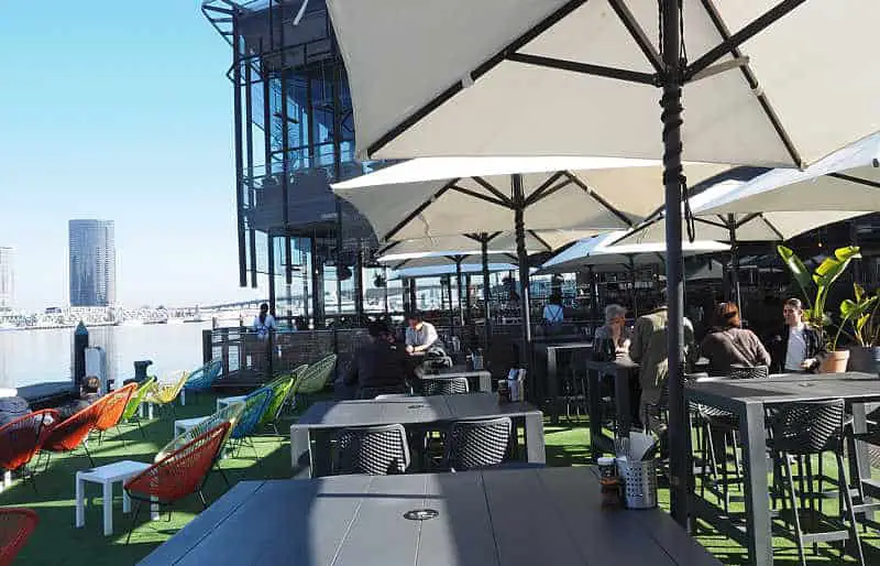 Outdoor dining area at Cargo Docklands with umbrellas, colourful chairs, and water views.