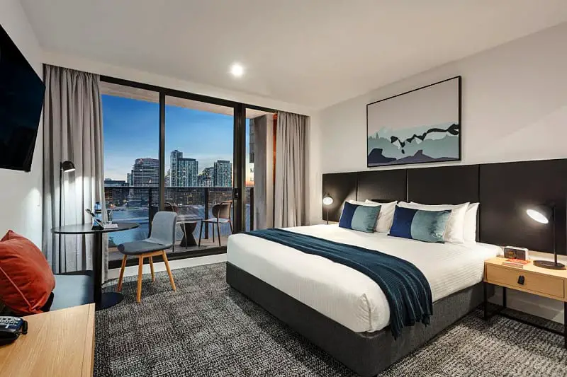 Guest room at Quest NewQuay Docklands with bed and views from floor to ceiling windows.