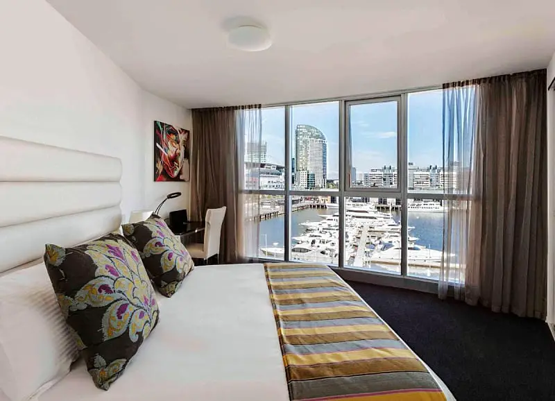 Guest room with bed and water views at The Sebel Melbourne Docklands.