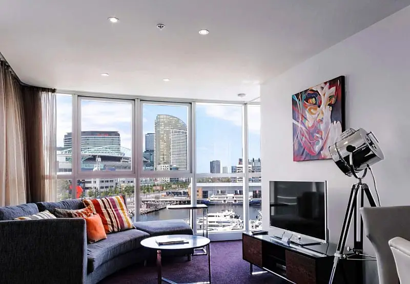 Guest room at The Sebel Docklands with a couch, TV and city views.