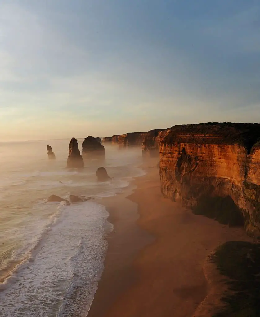 Image of the Great Ocean Road 12 Apostles at sunset with orange cliffs and fading blue skies.