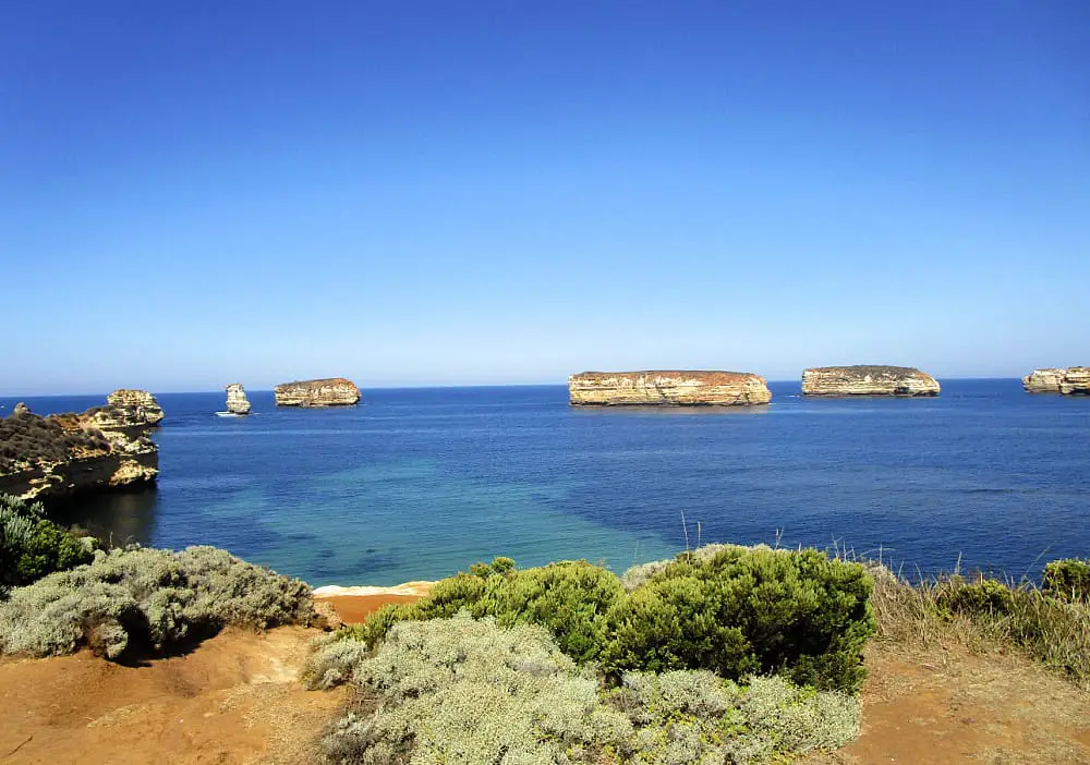 The Bay of Islands on the Great Ocean Road with green shrubs on the forefround and aquamarine sea and bright blue sky.