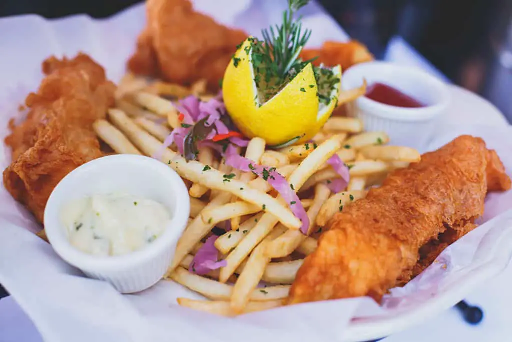 Serving of fish and chips with lemon and dipping sauces. 