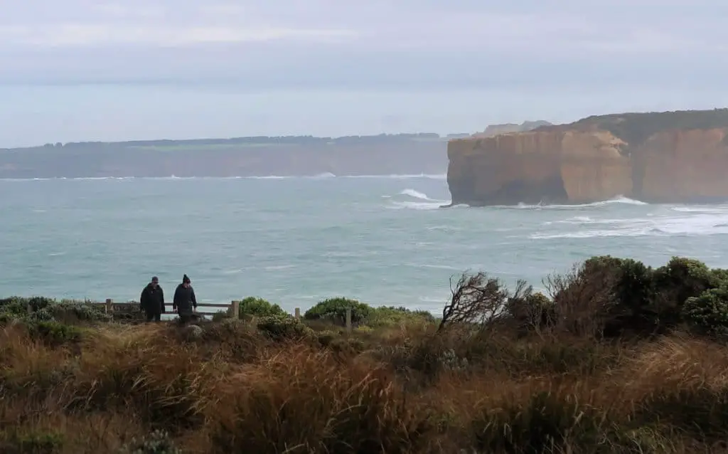 People walking along a trail on their 4 Day Great Ocean Road Tour with waves crashing into the cliffs in the background.