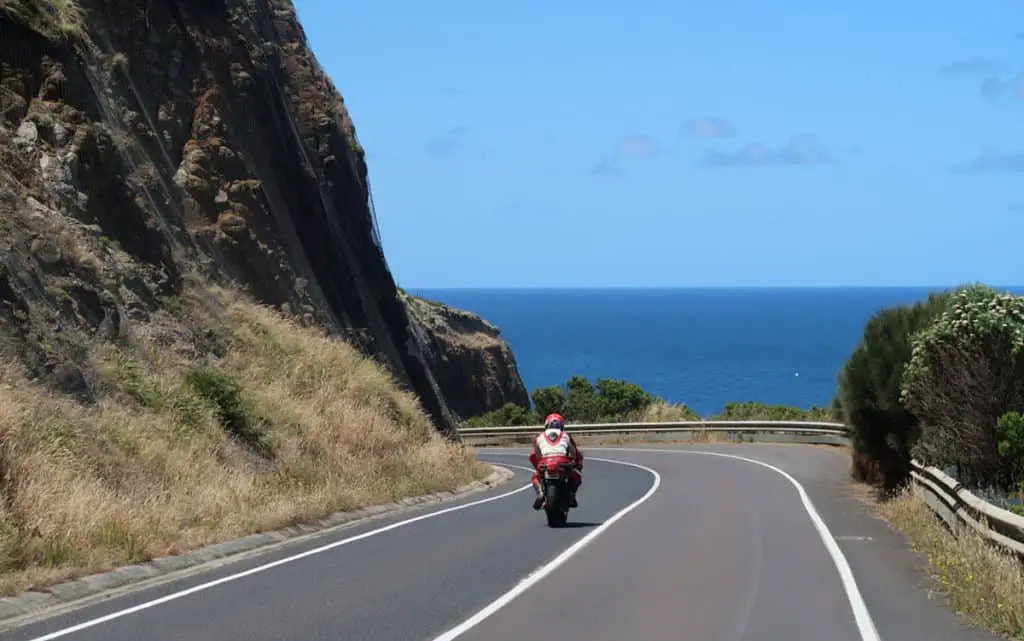 Motor bike and rider on the Great Ocean Road in Victoria with views of the ocean and blue skies.