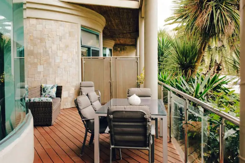Outdoor deck with couch and table and chairs surrounded by greenery at the Exclusive Anglesea River Beach Apartment. 