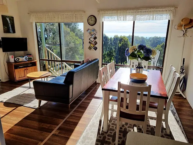 Living an dining area at Beech Forest Cottage with a dining table, couch, and bushland views.