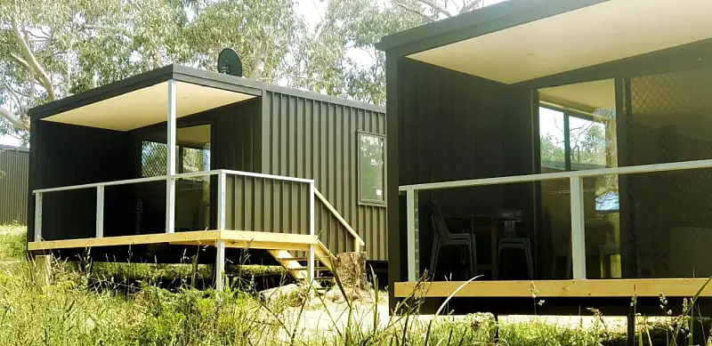 Modern black Bimbi Park cabins in the Otways with verandahs surrounded by forest. 