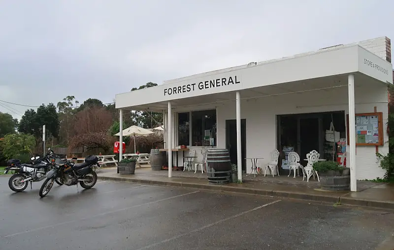Forrest General Store painted white with beer barrels for tables and outdoor dining and motor bikes in the car park on a cloudy day. A good place to stop while visiting the Otways attractions.