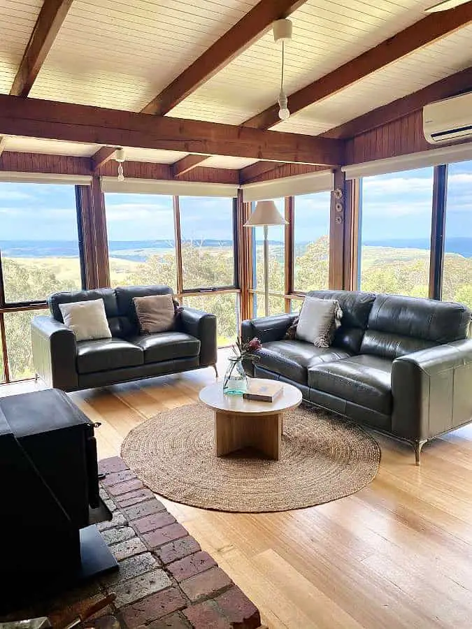 Living room at Glenaire Cottages in the Otways with floor to ceiling windows, a leather lounge suite and beautiful bushland views. 