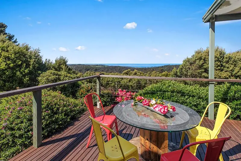 Balcony and outdoor table and chairs surrounded by trees with ocean views at Gone Surfin an Otways holiday house.