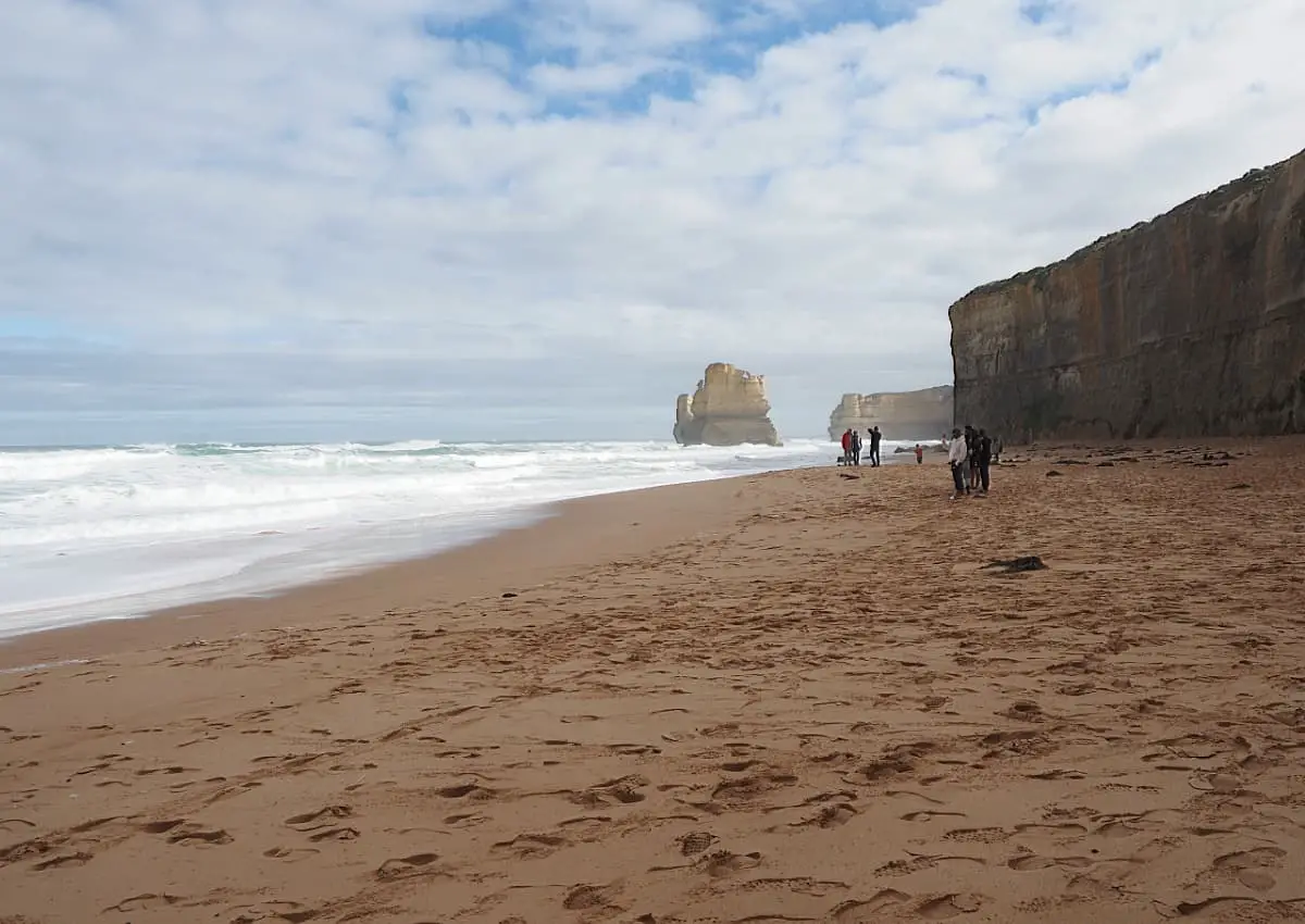People standing on a Great Ocean Road beach looking out to sea at a rock formation. Visiting the beach is a must on any Great Ocean Road 3 day itinerary.