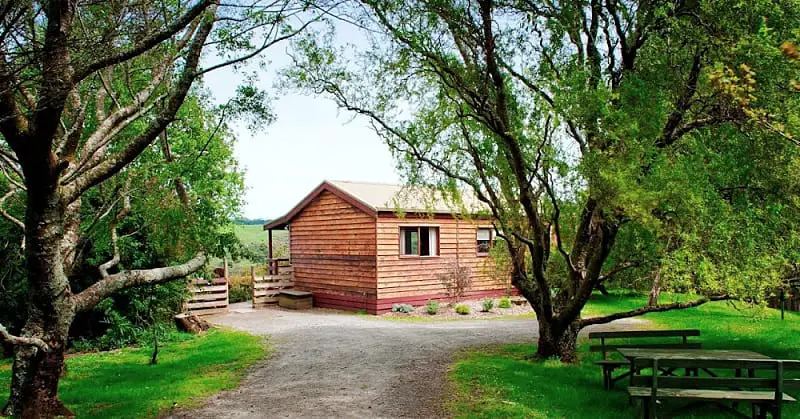 View of a cabin at Johanna River Farm and Cottages Otways accommodation surrounded by trees with a picnic table.