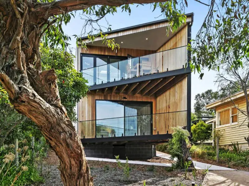 View of the architecturally designed Point Break Anglesea accommodation with two levels and balconies surrounded by gum trees.