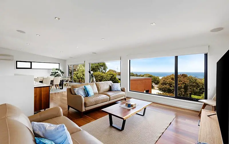 Living room with couches, a coffee table and floor to ceiling windows with ocean views at Seaside Haven some of the most beautiful accommodation Anglesea has to offer.
