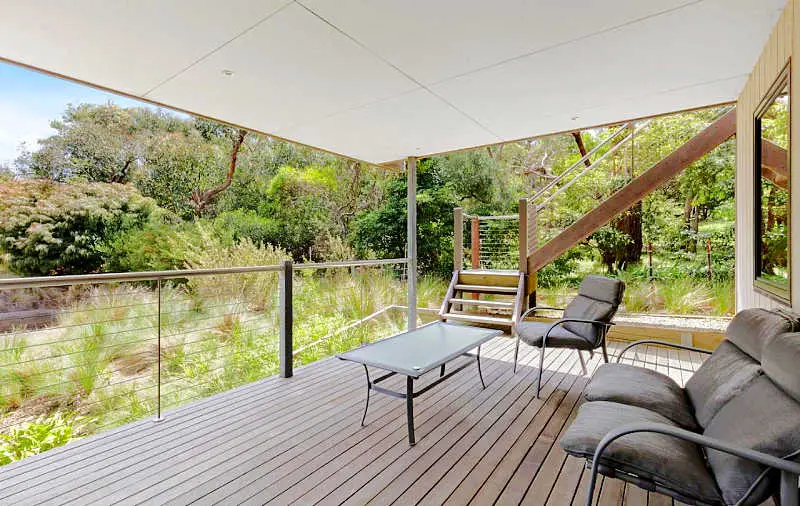 Wooden deck with a table and chairs surrounded by greenery at Seaside Haven in Anglesea Victoria.