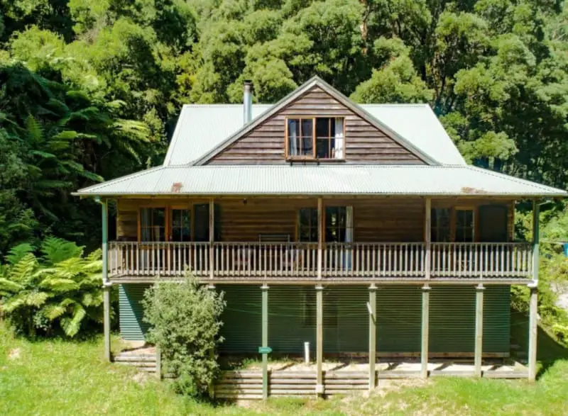 Two storey wood cabin Fern Cottage with wrap-around verandah surrounded by trees.  