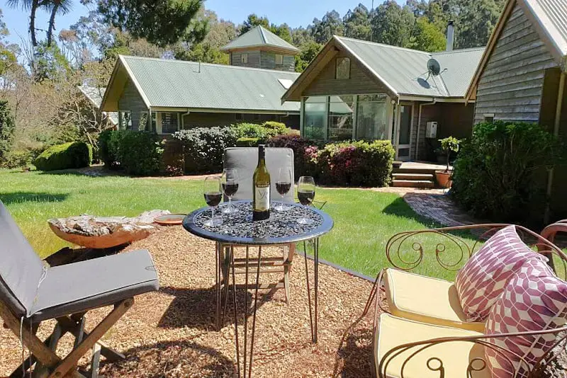 Picnic area with table and chairs and wine glasses with views of the cottages at The Otway Nest.