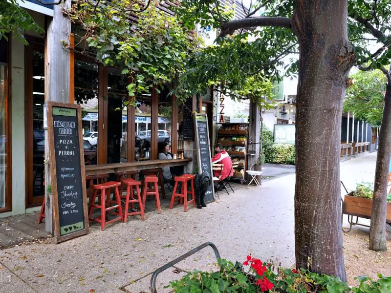 Outdoor dining area at Annie's Provedore with red stools, a leafy tree, and signage.