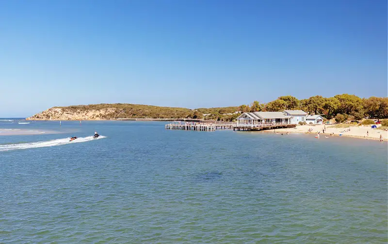 View of At The Heads restaurant from across the river with a speed boat on the water and coastal scrib in the background an iconic sight on the Bellarine Peninsula.